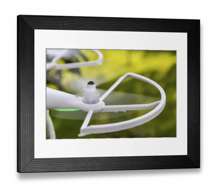 Framed Print : Blurred spinning propellers of a small helicopter drone (quadcopter) flying over green grassy surface
