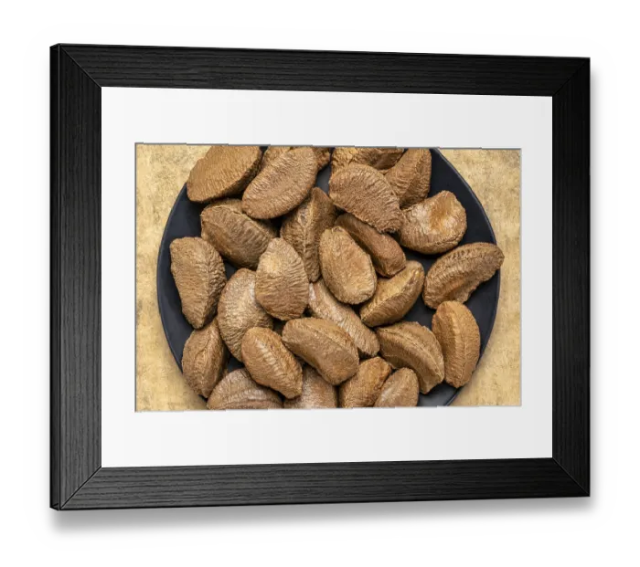 Framed Print : Brazilian nuts on a black plate against buckskin textured paper background with a copy space
