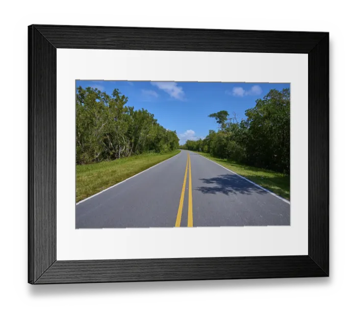 Framed Print : A country road leads through a wooded area under a clear sky