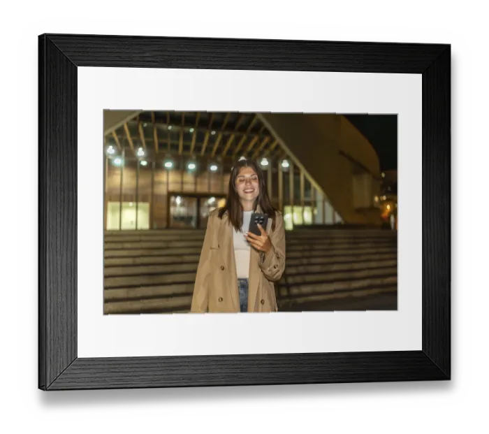 Framed Print : Young woman smiling while looking at her mobile phone outdoors