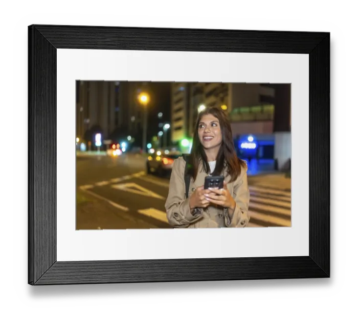 Framed Print : Young woman smiling and looking away while using a mobile phone on a pedestrian crossing