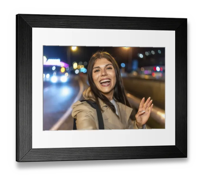 Framed Print : Young woman smiling and taking a nighttime selfie on a vibrant city street