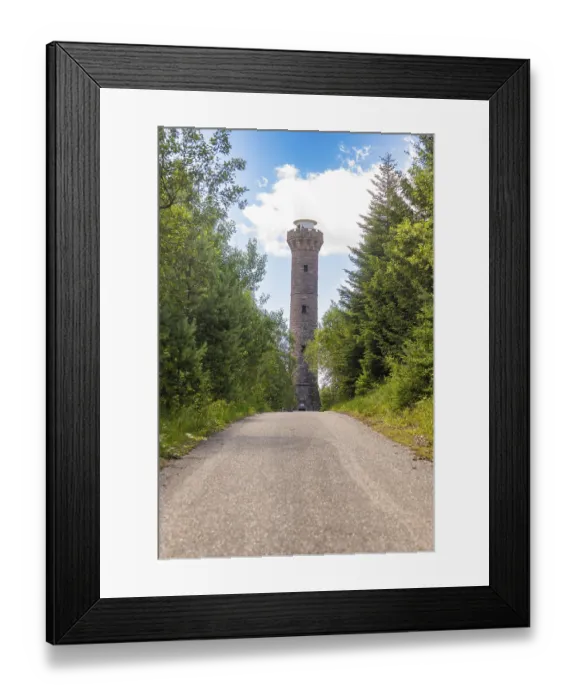 Framed Print : A tall stone tower rises into the sky above a forest path