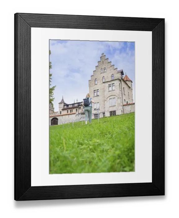 Framed Print : A woman walks up a grassy hill towards an imposing historic castle