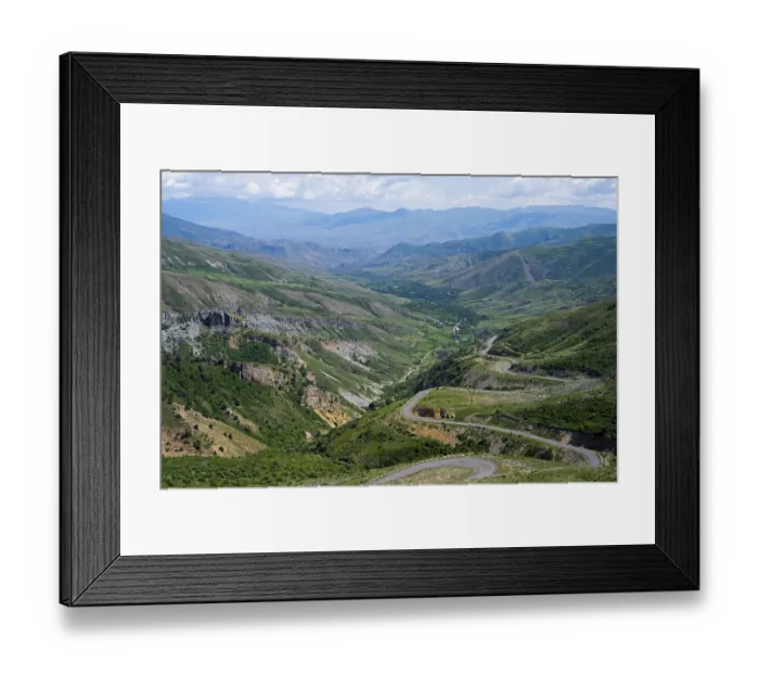 Framed Print : Winding roads lead down through a green valley into mountainous terrain under a clear sky