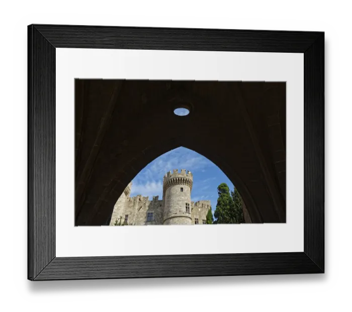Framed Print : View through a stone arch to a medieval castle with tower under a blue sky
