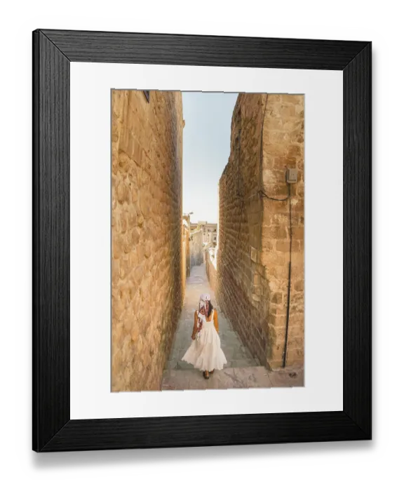 Framed Print : Traveler woman in white dress walking through narrow stone alley in historic city of Mardin Turkey with traditional