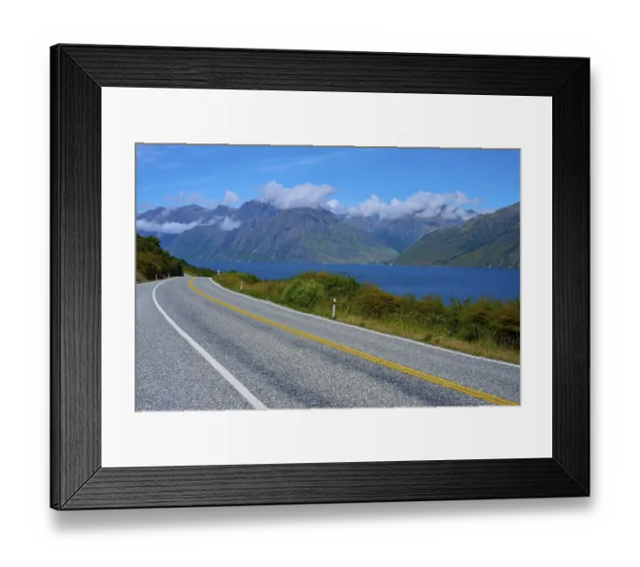 Framed Print : Winding road along a lake with mountains in the background