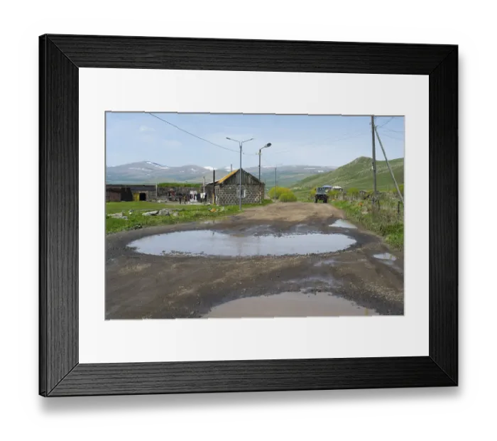 Framed Print : A muddy road with large puddles leads through a village with mountains in the background Framed Print : A muddy road with large puddles leads through a village with mountains in the background