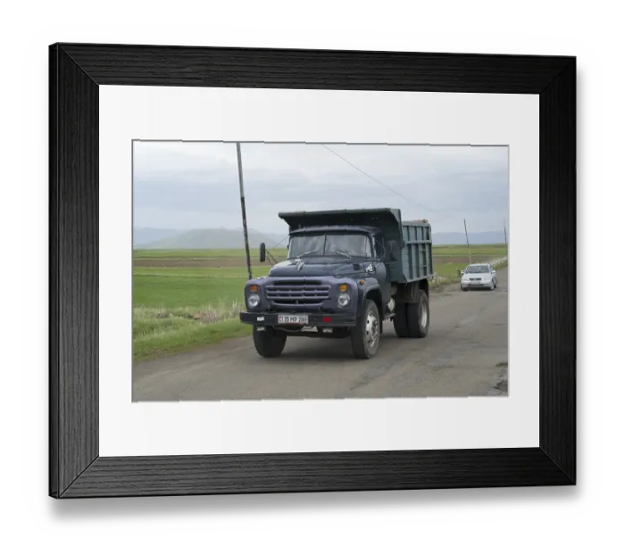Framed Print : A blue lorry with a trailer drives on a country road surrounded by green fields and mountains