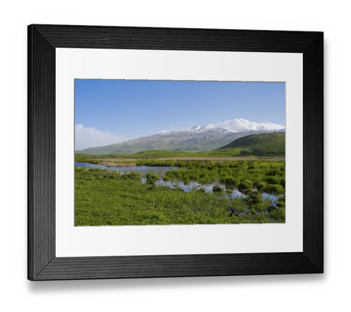 Framed Print : A river meanders through green hills in front of a mountain range with a slightly cloudy sky Framed Print : A river meanders through green hills in front of a mountain range with a slightly cloudy sky