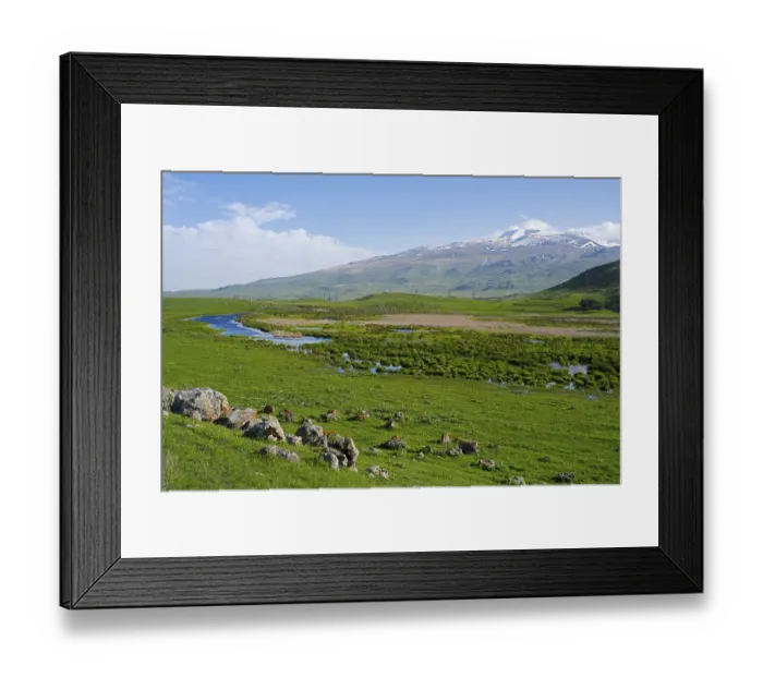 Framed Print : Green meadows with a meandering stream and a mountain range in the background under a clear sky