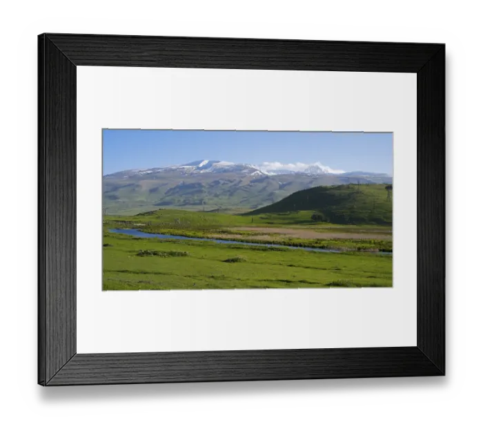 Framed Print : A wide view over a green valley with snow-capped mountains under a clear sky