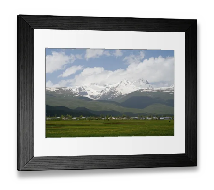Framed Print : Green meadows in front of snow-covered mountains under a cloudy blue sky