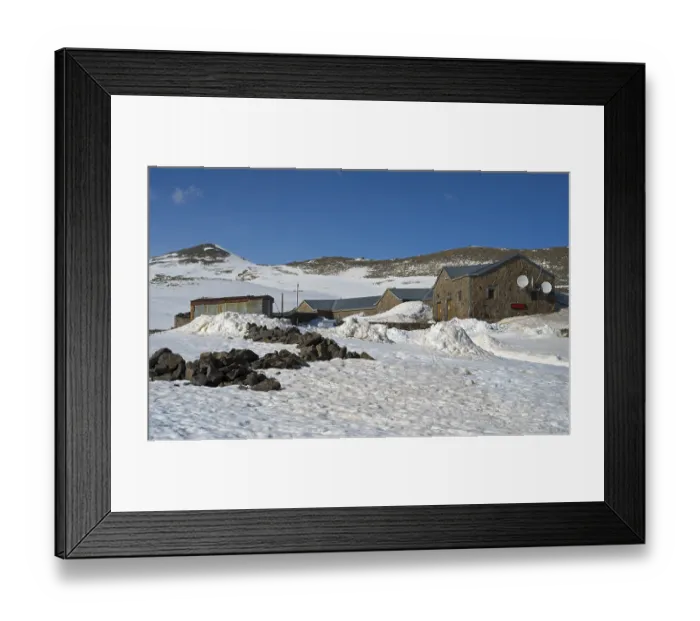 Framed Print : Snow-covered landscape with stone and metal buildings under a clear blue sky