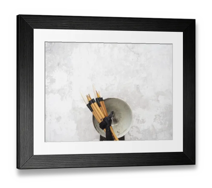 Framed Print : Multiple calligraphy brushes tied together with a black ribbon are resting on a ceramic bowl