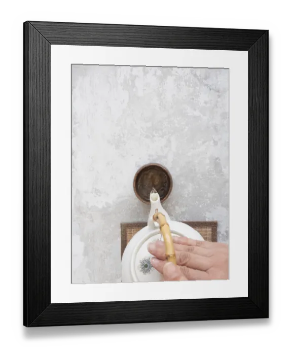 Framed Print : Hand gracefully pours tea from a white ceramic teapot with bamboo handle into a small brown bowl on a textured gray Framed Print : Hand gracefully pours tea from a white ceramic teapot with bamboo handle into a small brown bowl on a textured gray
