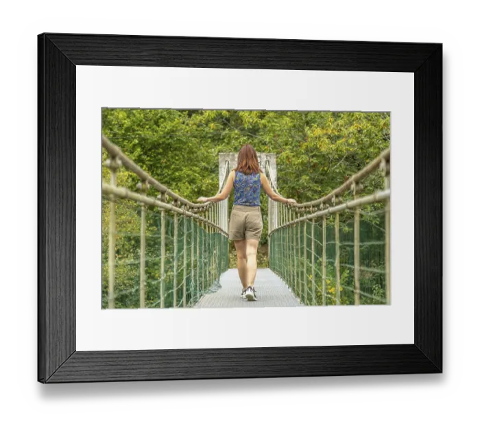 Framed Print : Female tourist enjoying a peaceful walk across a metallic hanging bridge