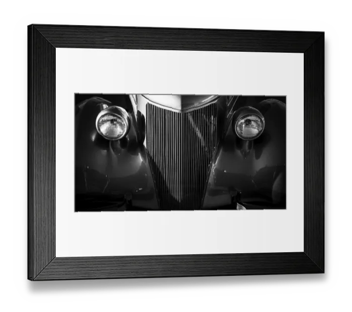 Framed Print : Front view of a vintage car in black and white with prominent headlights and grille in St
