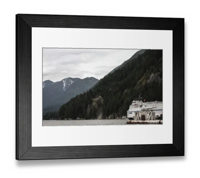 Framed Print : A ferry navigating near mountains covered in dense forest under cloudy skies at Horseshoe Bay