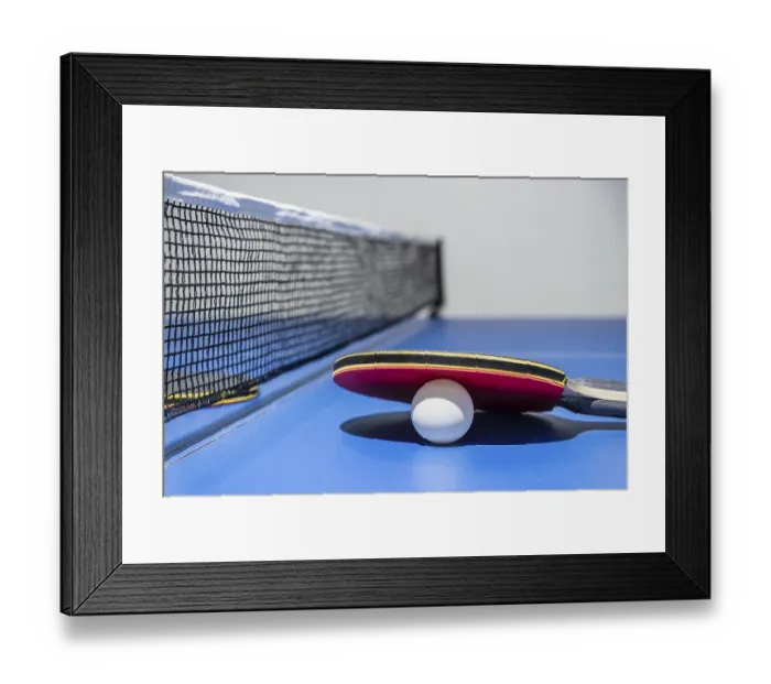 Framed Print : Closeup red table tennis racket and a white ball on the blue ping pong table with a black net Framed Print : Closeup red table tennis racket and a white ball on the blue ping pong table with a black net