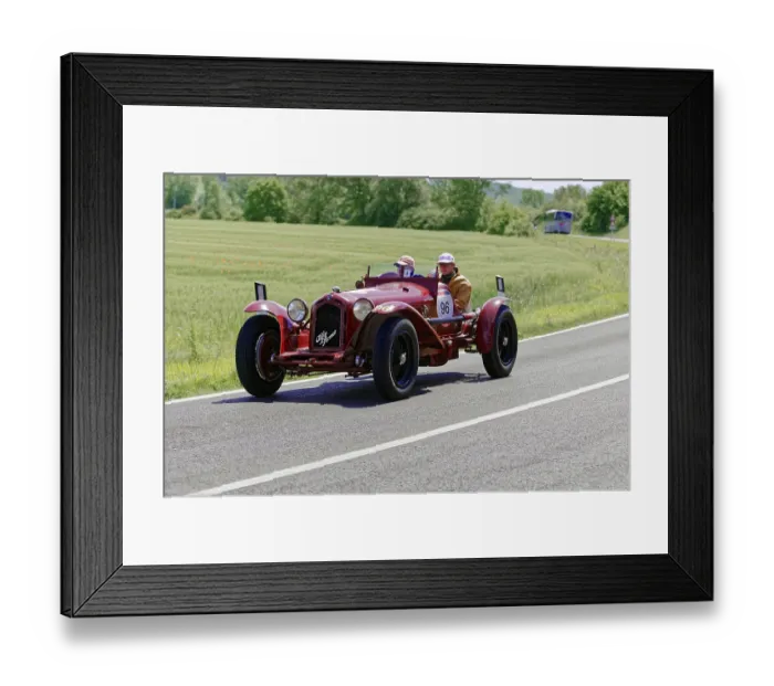 Framed Print : A red classic car drives on a country road through a green landscape