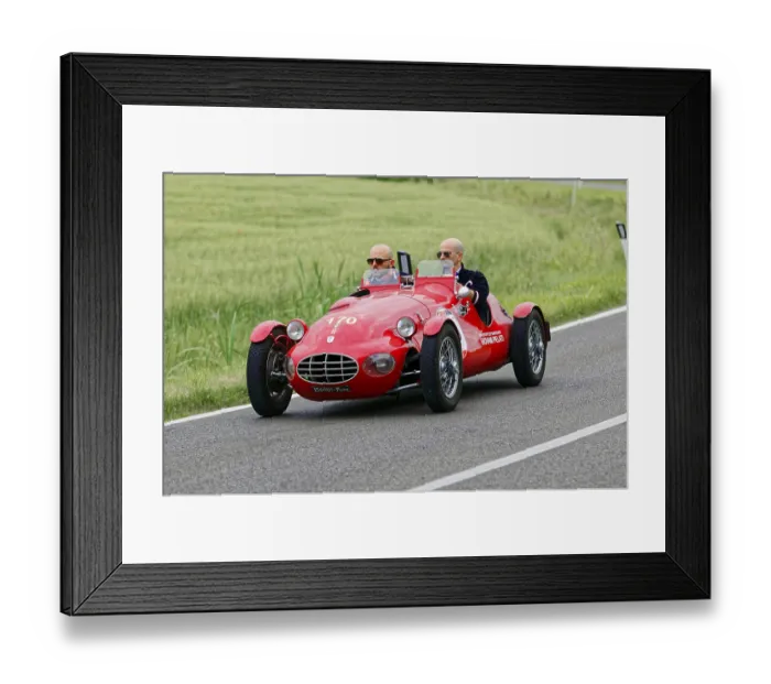 Framed Print : An open red sports car with two drivers drives through a green landscape
