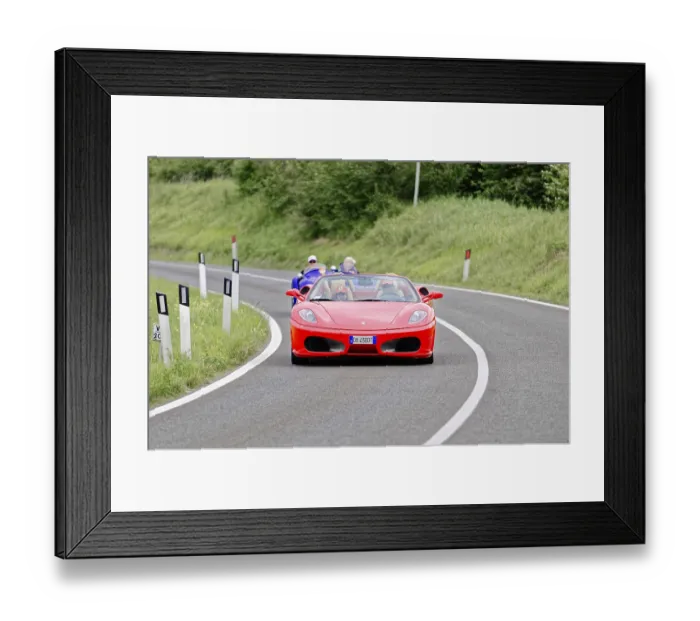 Framed Print : Red Ferrari convertible on winding road surrounded by green landscape