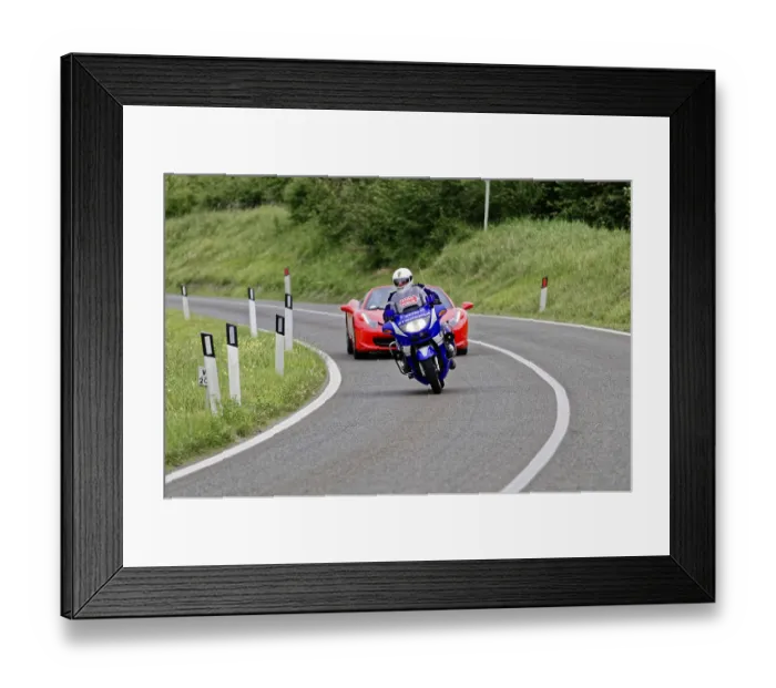 Framed Print : Blue motorbike takes a bend in front of a red Ferrari convertible on a country road