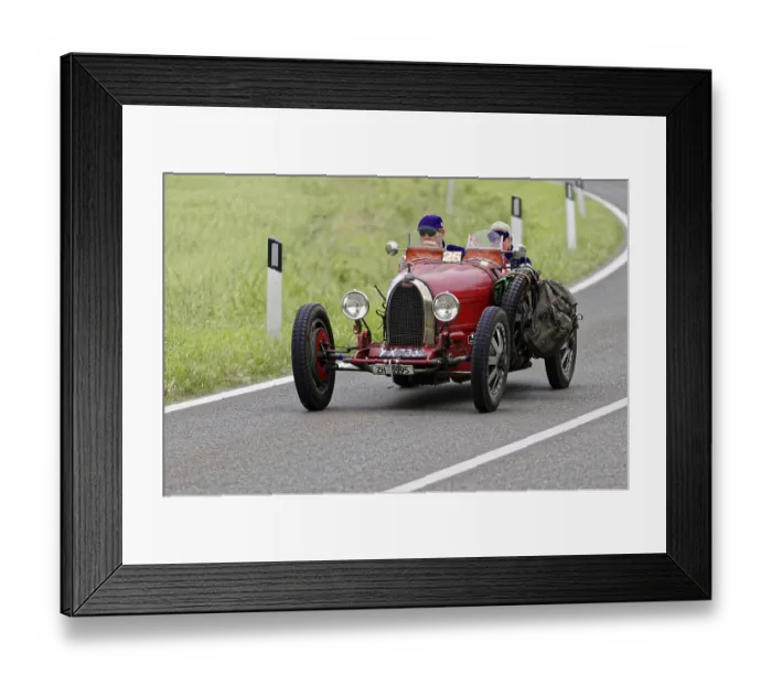Framed Print : Two people in a red vintage car with racing equipment on a country road