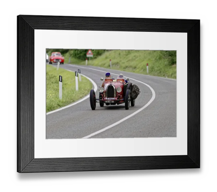 Framed Print : Two people with helmets in a red vintage car on a winding road