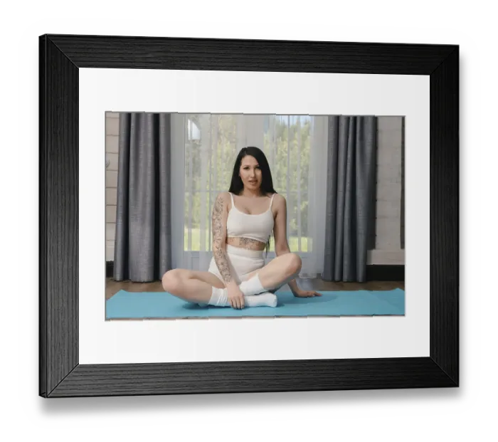 Framed Print : A young woman with dark hair and a tattoo on her arm sits in a yoga pose on a blue mat