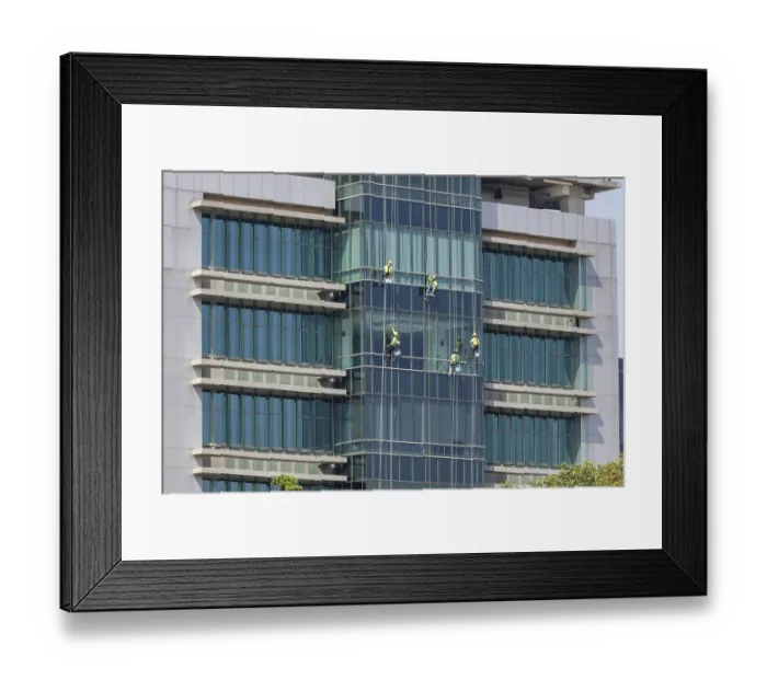 Framed Print : Window cleaners work as a team to clean the glass front of a hospital in downtown Bangkok