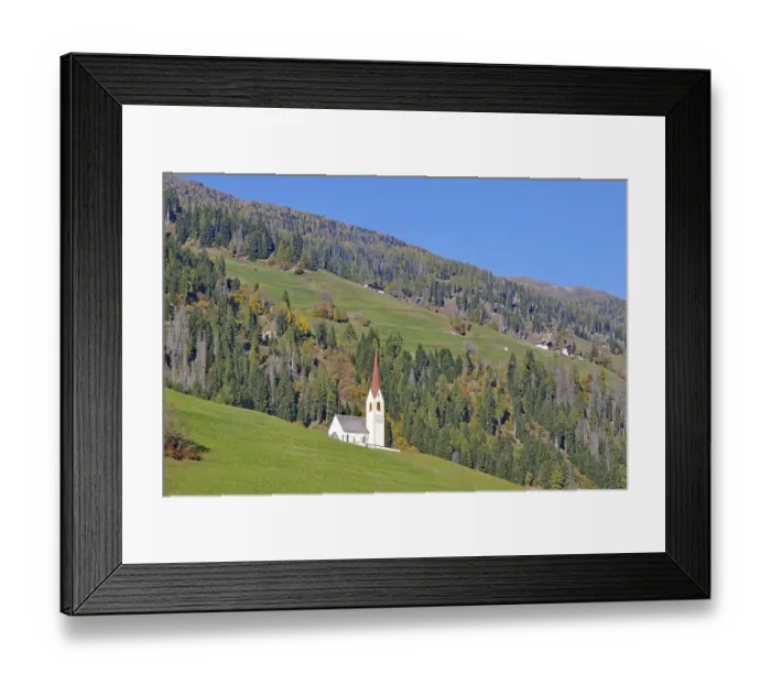 Framed Print : Lonely church with red tower on green alpine slope under bright blue sky