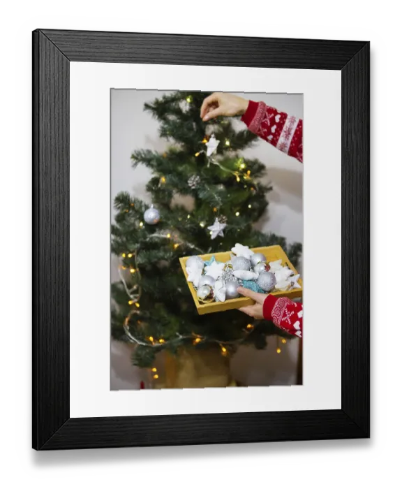 Framed Print : A happy girl in a red sweater holds a tray of Christmas toys and decorates the Christmas tree at home for Christmas