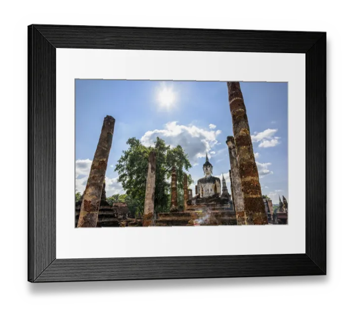 Framed Print : Ancient Buddha statue sitting among the ruins under the bright sun of Wat Maha That temple in Sukhothai Historical Park