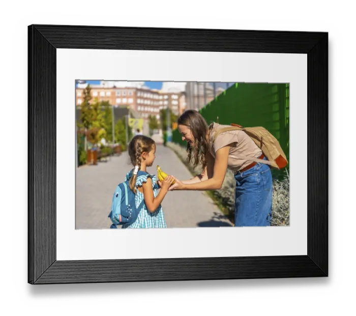 Framed Print : Mother smiles as she hands her schoolgirl a banana on a sunny walk