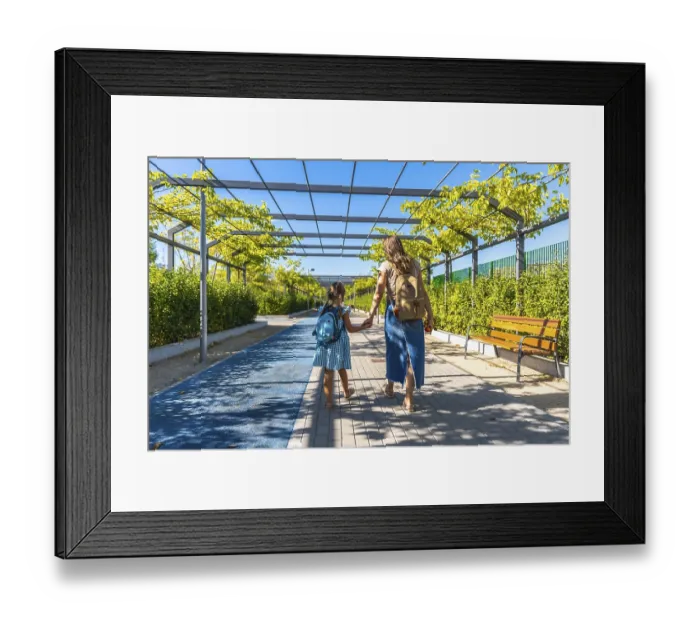 Framed Print : Mother and daughter walk hand in hand along an urban park path with backpacks Framed Print : Mother and daughter walk hand in hand along an urban park path with backpacks
