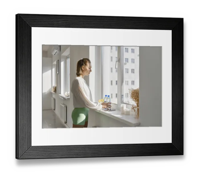 Framed Print : A young woman stands by a large window