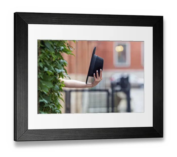 Framed Print : A person extends their arm to hold a black hat near a lush green plant wall in the city