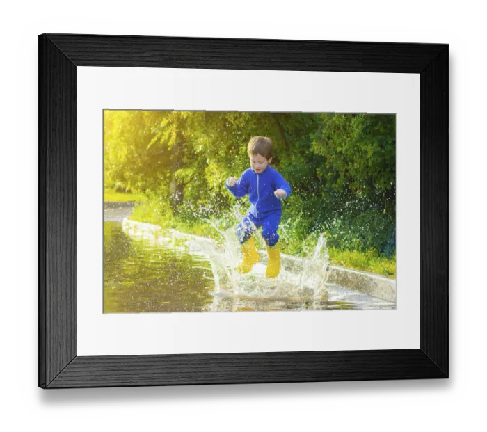 Framed Print : A happy boy in rubber boots jumps in puddles