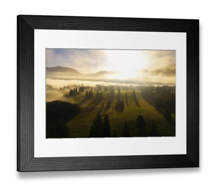 Framed Print : Morning light breaks through fog in picturesque grassy landscape with mountains in the background
