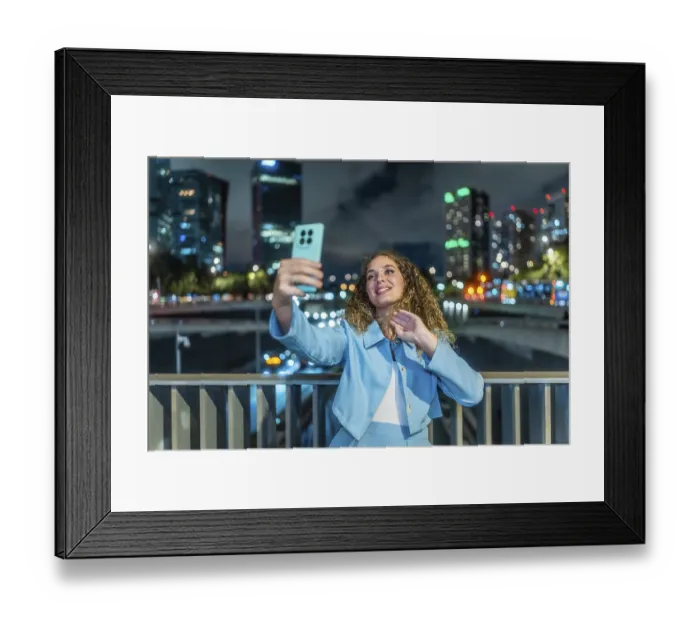 Framed Print : Young woman with curly hair and blue suit taking a selfie with her smartphone on a city bridge at night Framed Print : Young woman with curly hair and blue suit taking a selfie with her smartphone on a city bridge at night