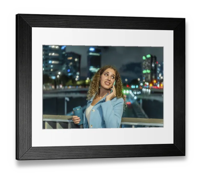 Framed Print : Young woman with curly hair talking on phone with a worried expression while holding a reusable cup Framed Print : Young woman with curly hair talking on phone with a worried expression while holding a reusable cup