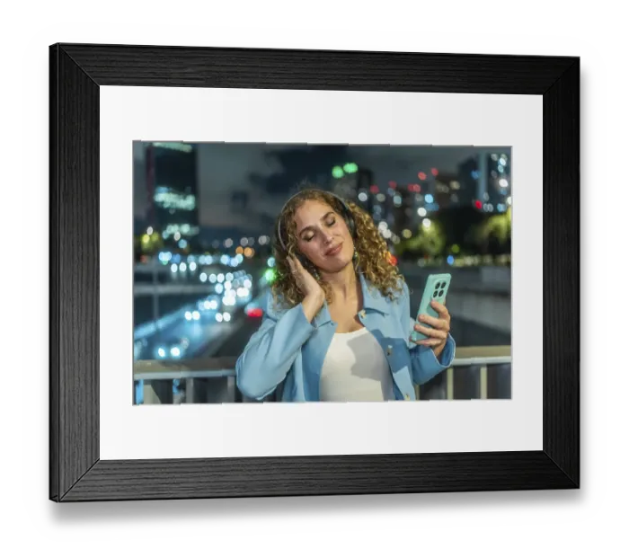 Framed Print : Young woman with curly hair finding joy and relaxation listening to music using headphones and a smartphone