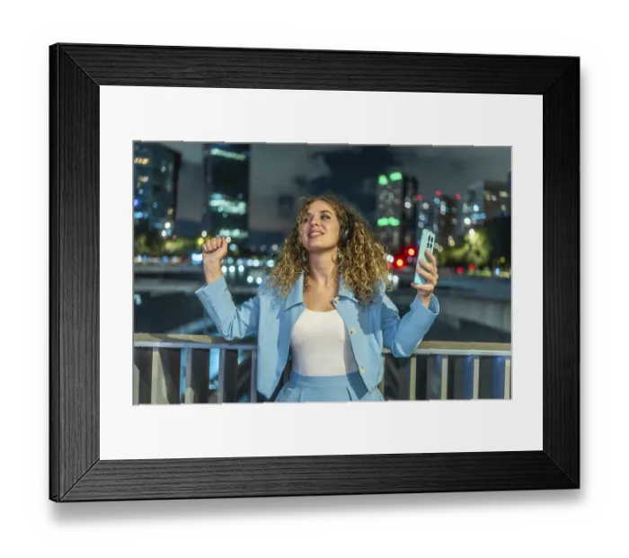 Framed Print : Young woman with curly hair wearing headphones and holding a smartphone Framed Print : Young woman with curly hair wearing headphones and holding a smartphone
