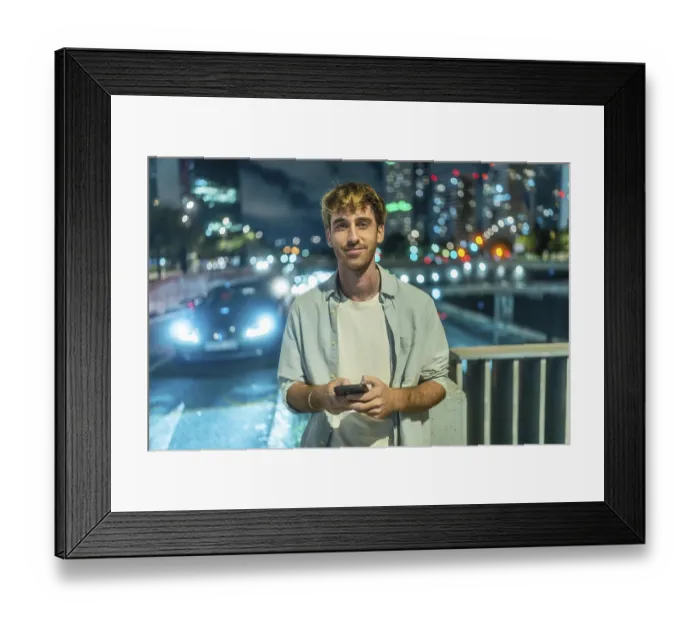Framed Print : Young man standing outdoors at night smiling at his smartphone