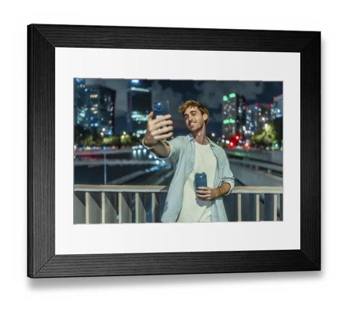 Framed Print : Young man smiling and taking a selfie with a smartphone while holding a reusable coffee cup