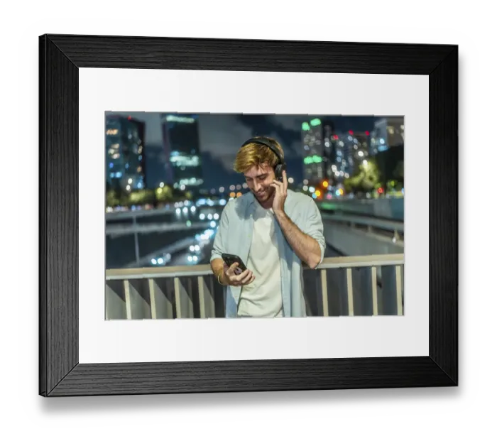 Framed Print : Young man smiling and listening to music through wireless headphones
