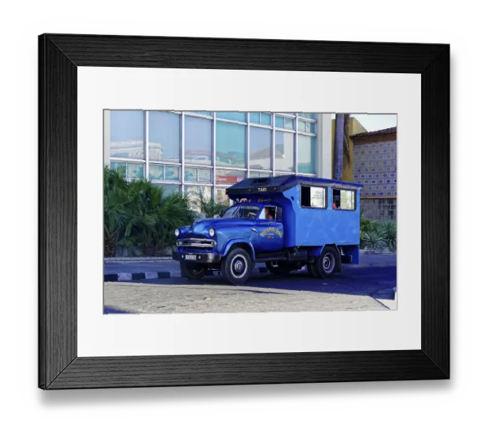 Framed Print : Santiago de Cuba, A blue vintage taxi passes in front of a modern building